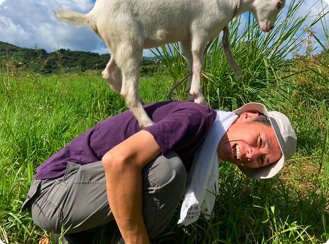 ヤギが背中に載っている状態の笑顔の男性の写真