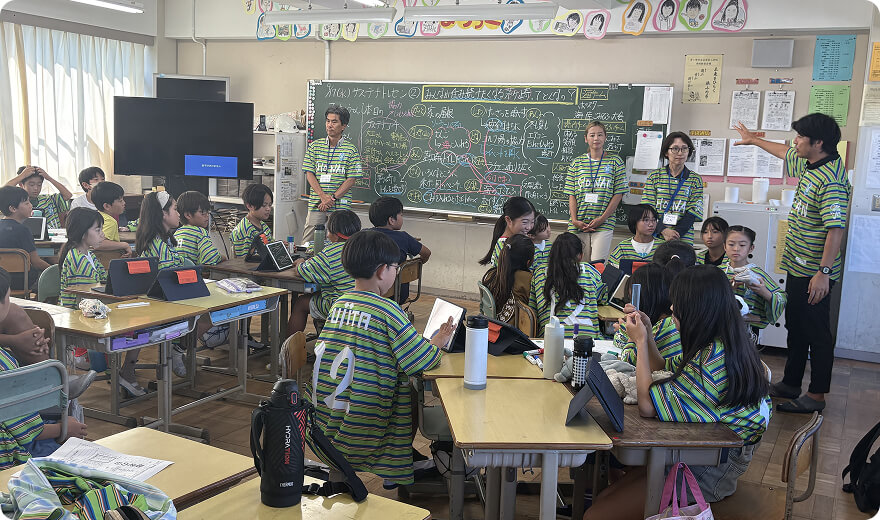 教室でユニフォームを着て話をする大人たちとそれを聞く子どもたちの写真