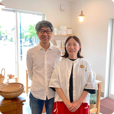 お店のようなところで笑顔で立つ夫婦の写真