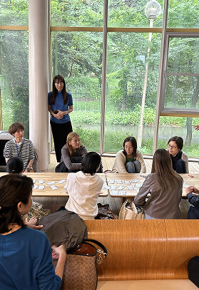 机に集まって何かしている人たちと立ってそれを見つめる人の写真