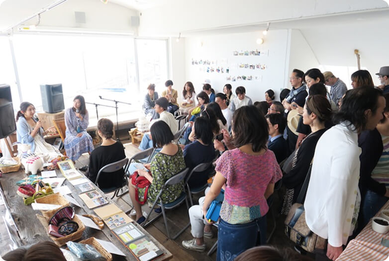 前で話をする女性2人と話を聞く人たちの写真