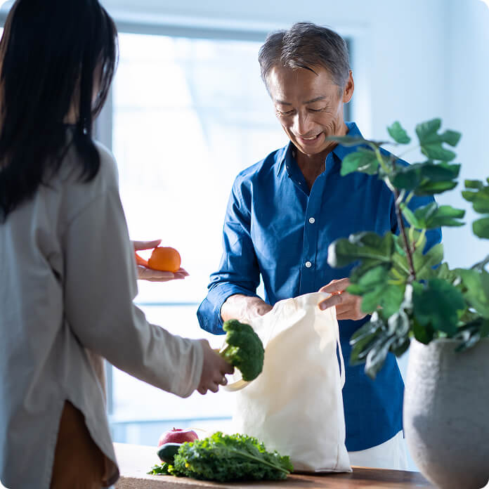 布のバッグから野菜を取り出す男性と、その野菜を持つ後ろ姿の女性の写真